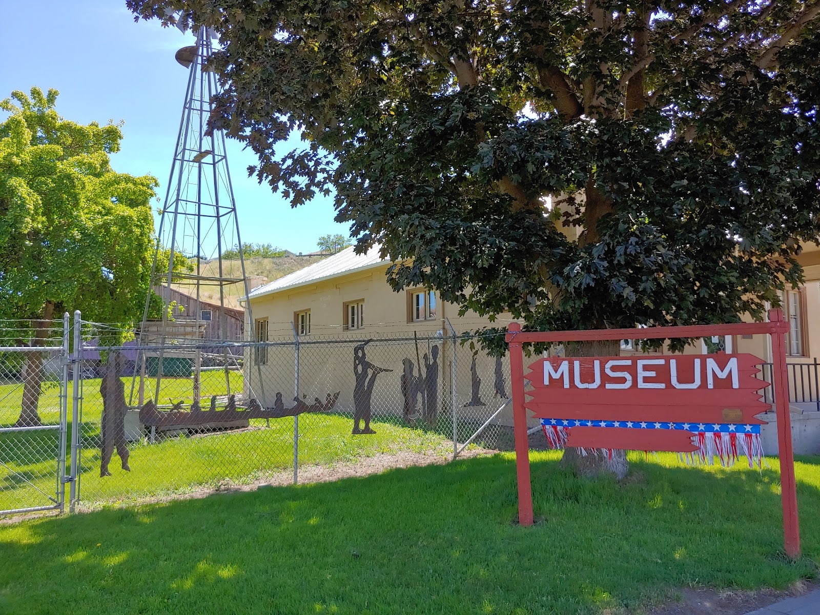 Red Museum sign on the lawn at the Asotin County Museum, with a windmill and historic buildings behind