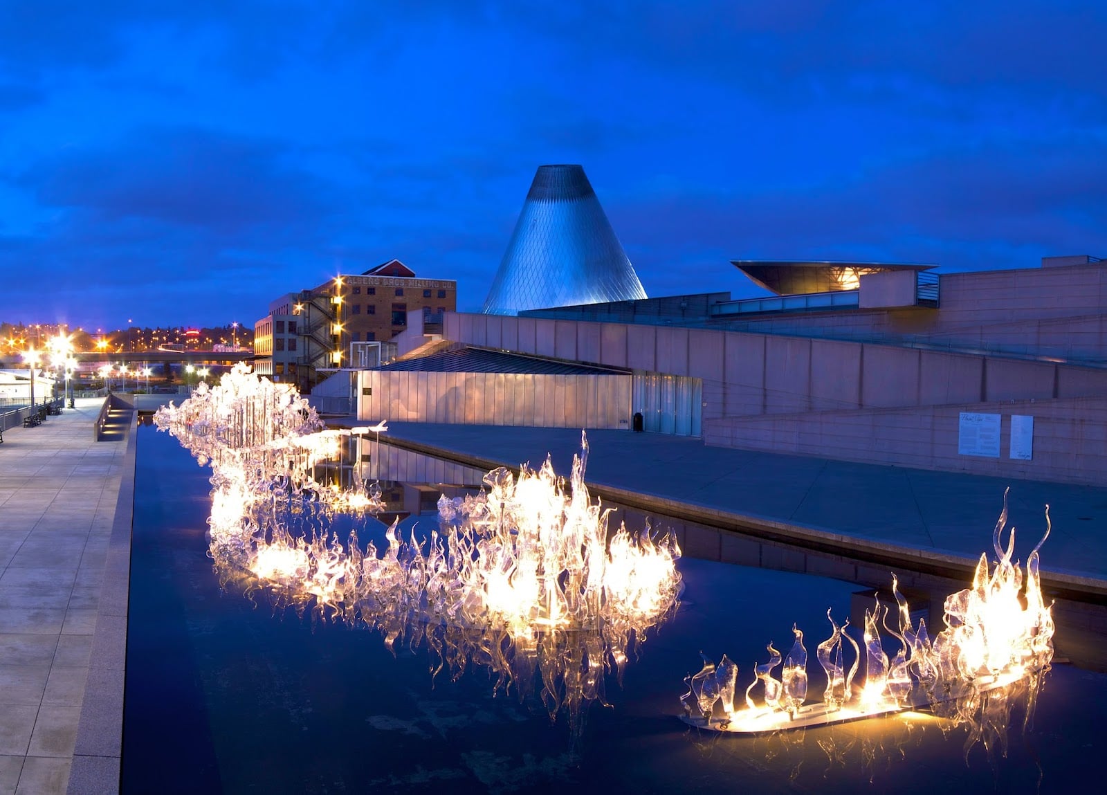 Glass sculptures lit at dusk in the reflecting pool outside the Museum of Glass, with its steel cone behind