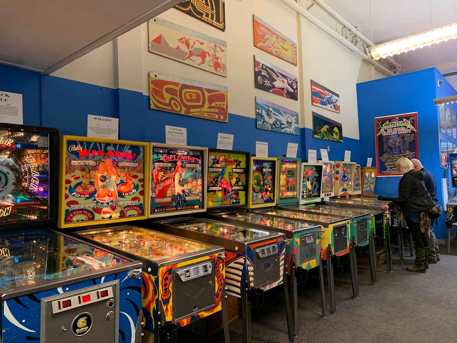 Rows of vintage pinball machines under painted backglass art at the Seattle Pinball Museum