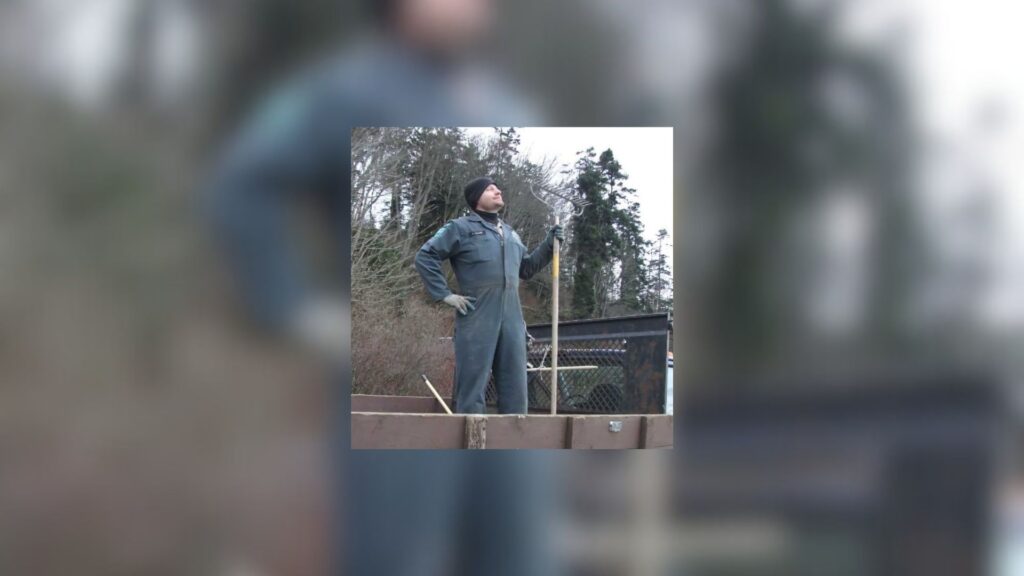 Washington State Parks Wallace Falls ranger Kevin Leese standing in the back of a work truck, holding a rake in a confident pose during park maintenance, with winter trees in the background.