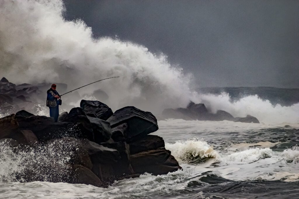 An angler on the rocks as a storm wave breaks behind him on the Washington coast at Ocean Shores