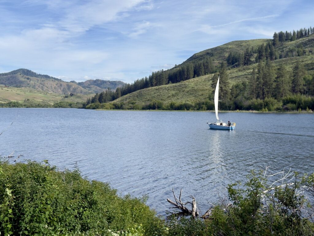 A small sailboat under sail on Pearrygin Lake, with green hills rising behind the far shore
