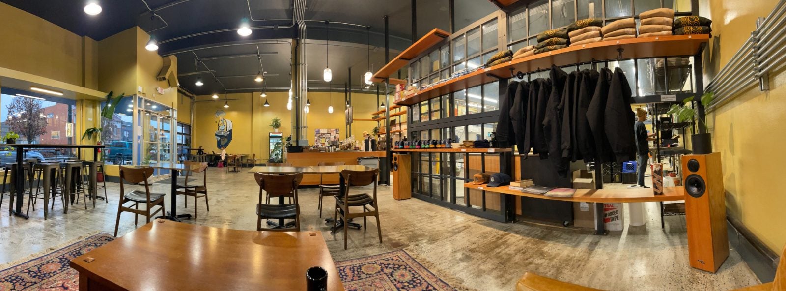 The yellow cafe inside Bluebeard Coffee Roasters on South Tacoma Way in Tacoma, with wood shelves of merchandise and the production area behind glass doors