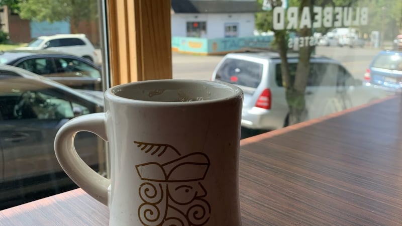 A Bluebeard Coffee Roasters mug on the window counter at the Sixth Avenue cafe in Tacoma, with the shop name lettered on the glass