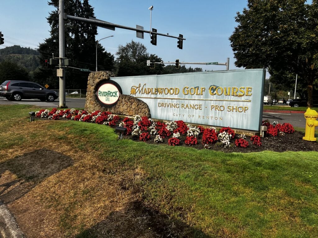 The Maplewood Golf Course entrance sign on Maple Valley Highway with red and white flowers