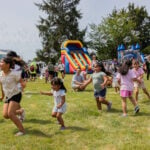 Kids chase bubbles across the lawn at Kids Day in Auburn, with bounce houses behind them