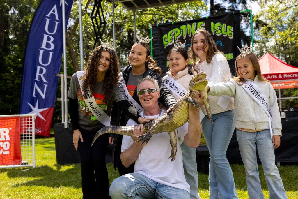 Miss Auburn and her court in crowns and sashes pose with a man holding an alligator at Pet Palooza in Auburn