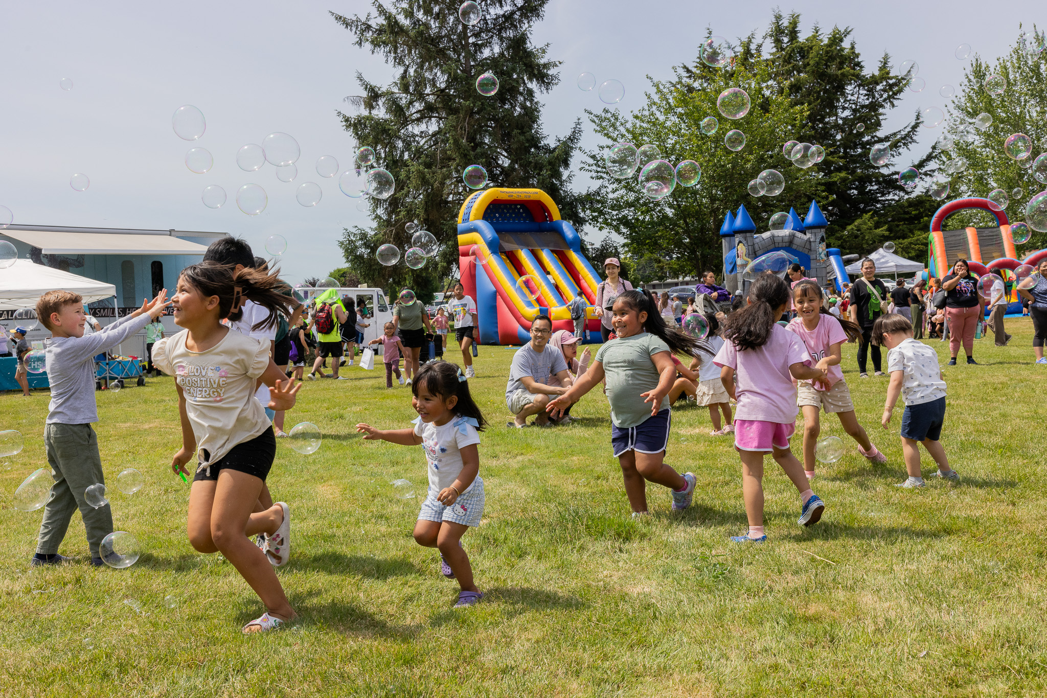 Kids chase bubbles across the lawn at Kids Day in Auburn, with bounce houses behind them