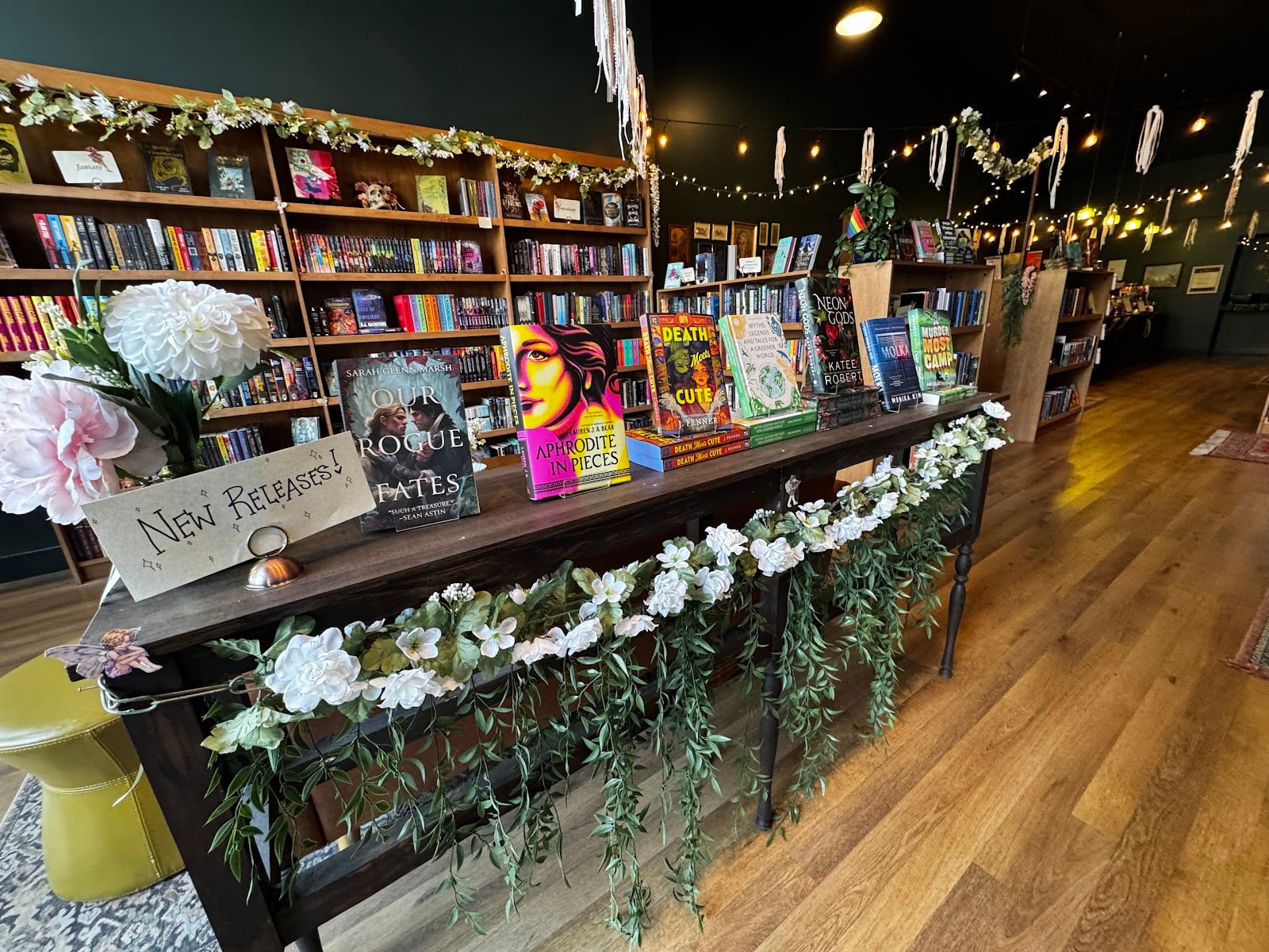 A new releases table and dark wood shelves strung with lights at Jupiter's Eye Book Cafe