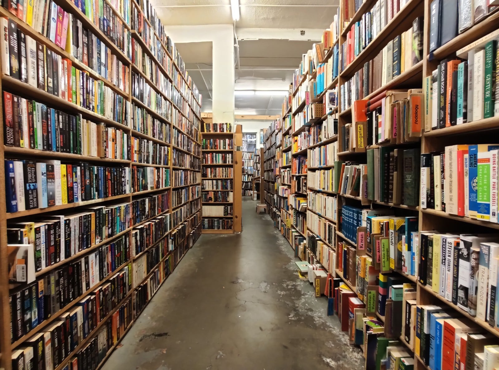 A long aisle of floor to ceiling used book shelves inside Magus Books in the University District