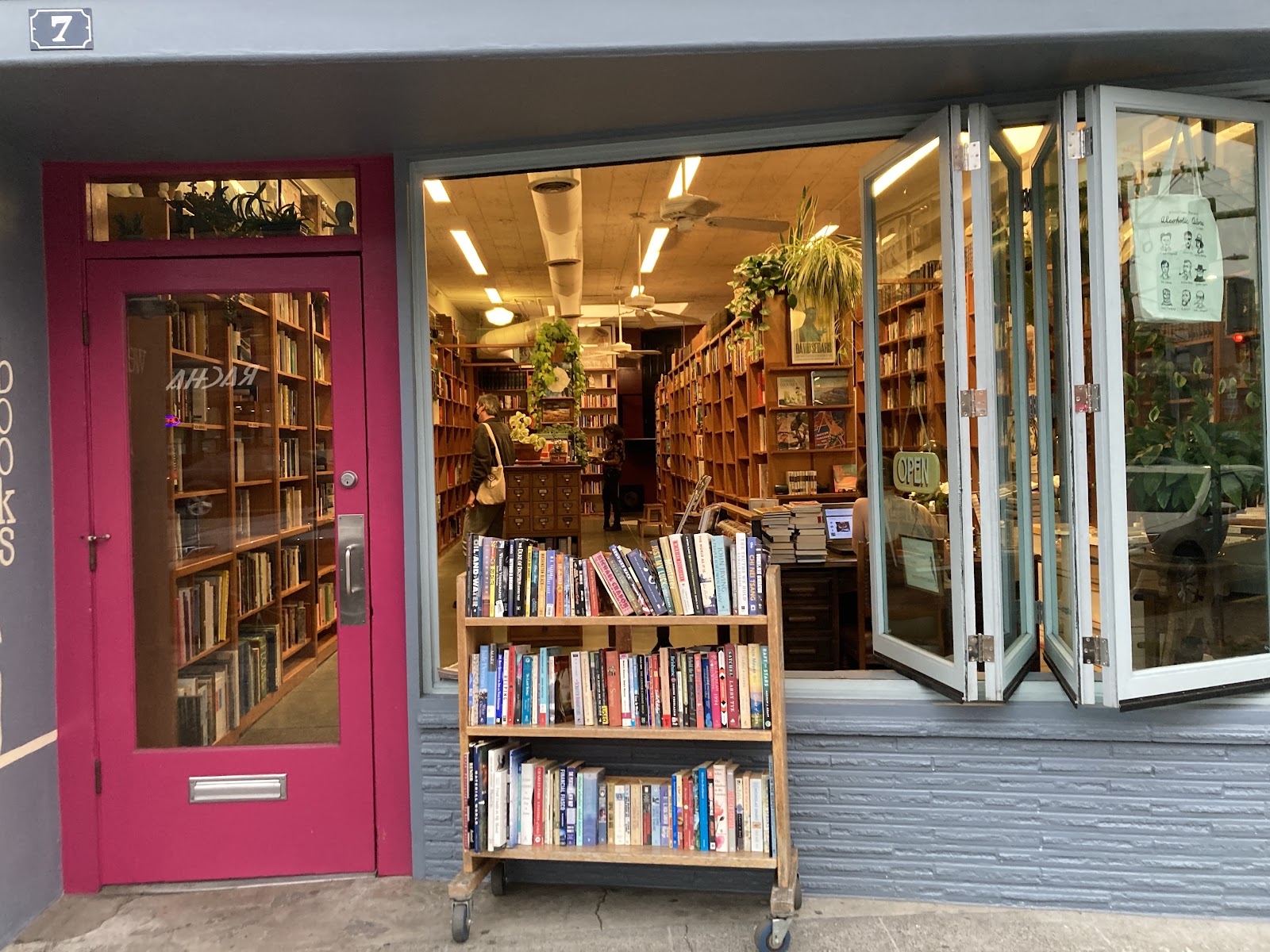 The pink door and folding front windows of Mercer Street Books with a cart of books by the entrance